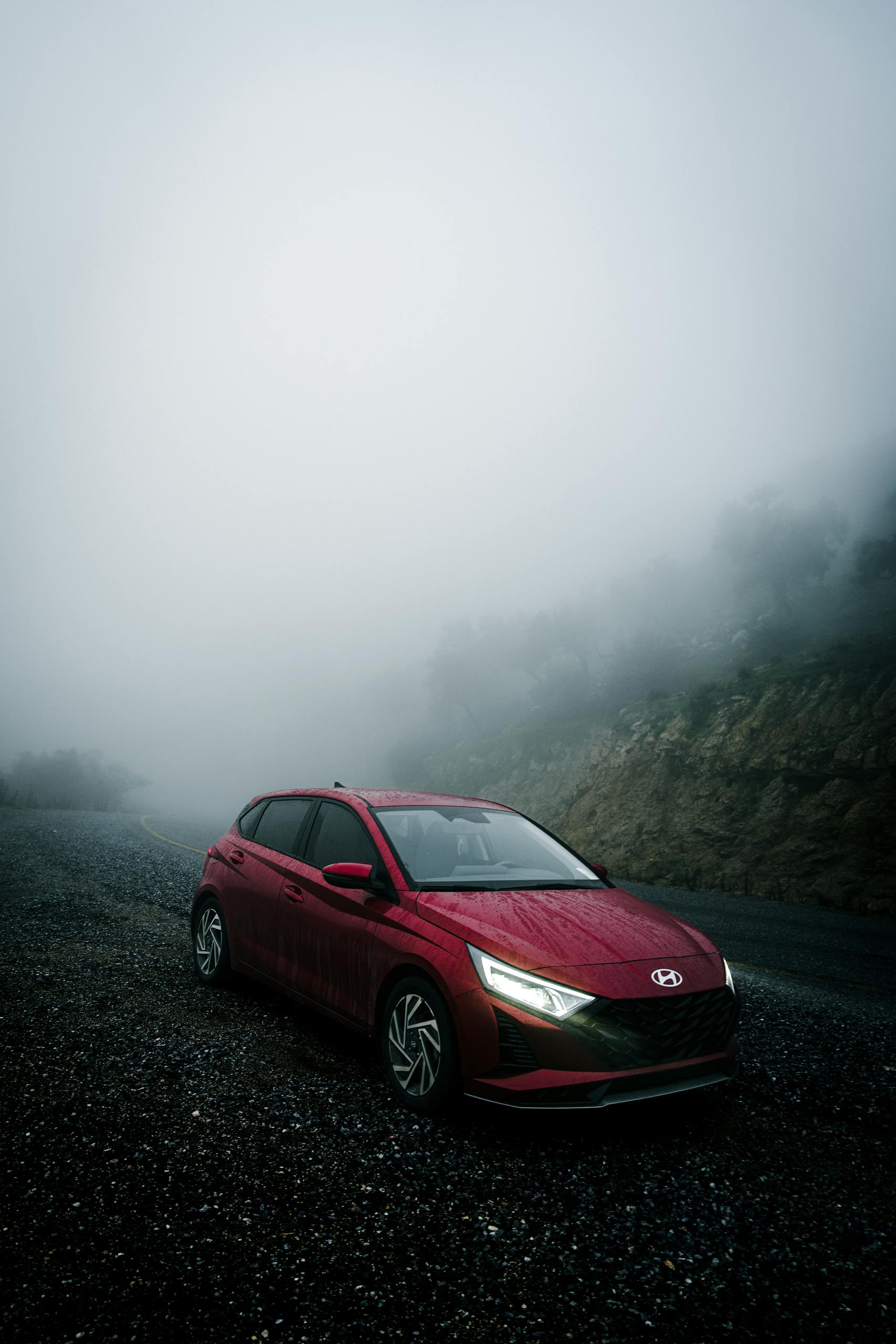 A red car parked on a misty mountain road, surrounded by dense fog and dramatic scenery.