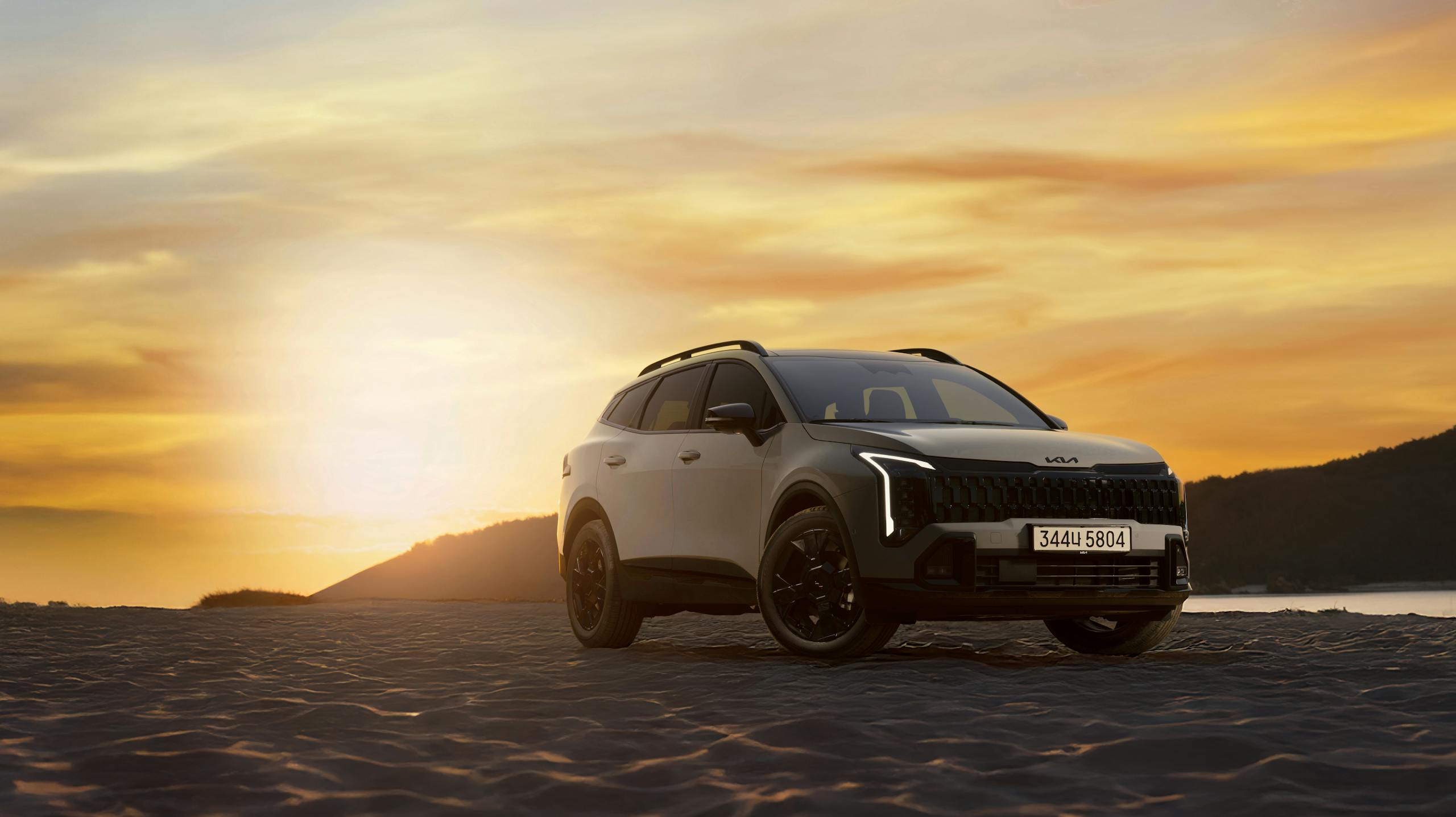 A stylish SUV parked on a sandy beach with a vibrant sunset in the background.