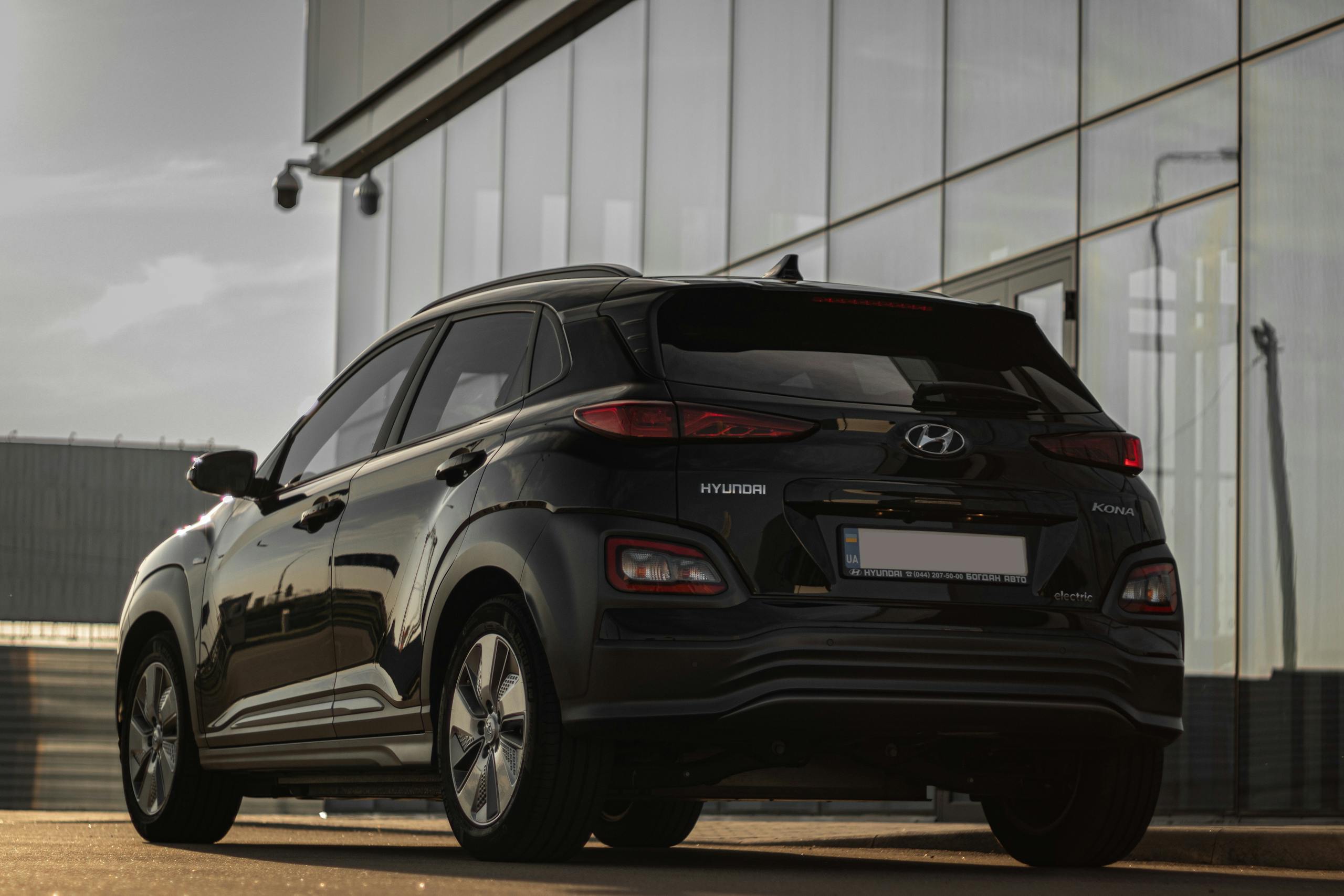 Rear view of a black Hyundai Kona parked next to a contemporary glass building reflecting urban architecture.